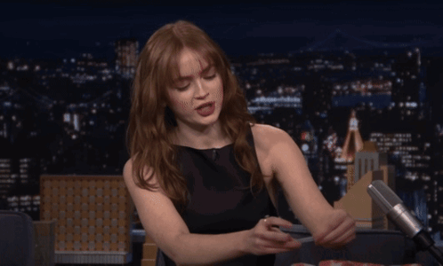A Woman In A Black Dress Is Sitting In Front Of A Microphone At Night GIF