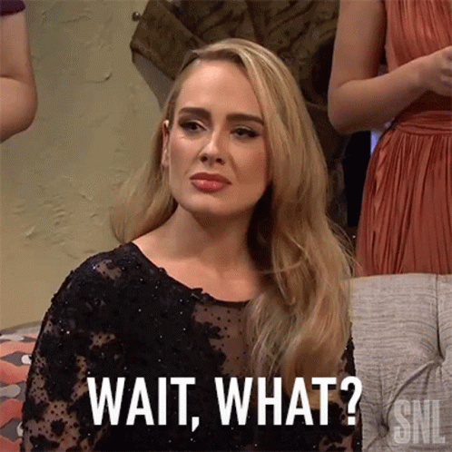 A Woman In A Black Dress Is Sitting On A Couch And Says Wait What . GIF