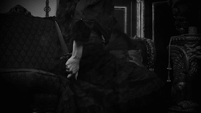 A Woman In A Black Dress Is Sitting On A Couch In A Room . GIF