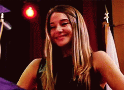 A Woman In A Black Dress Is Smiling In Front Of A Man In A Graduation Cap And Gown . GIF