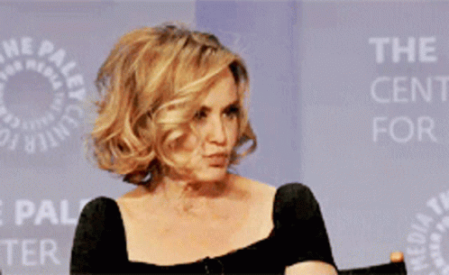 A Woman In A Black Dress Is Smiling In Front Of A Sign That Says The Paley Center GIF