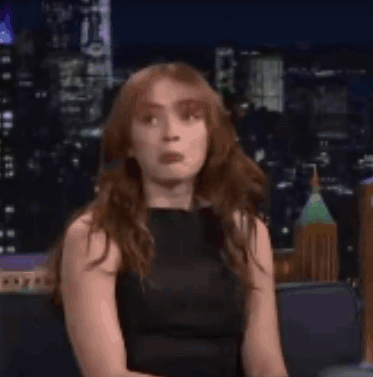 A Woman In A Black Dress Is Smiling While Sitting On A Couch In Front Of A City Skyline . GIF