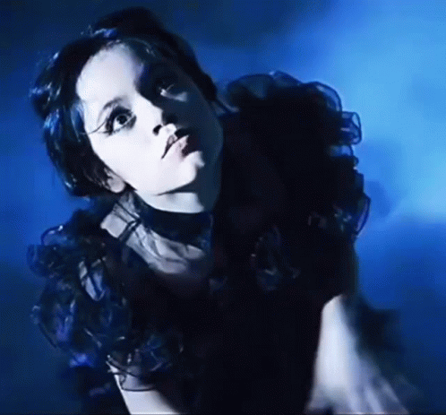 A Woman In A Black Dress Is Standing In A Dark Room . GIF