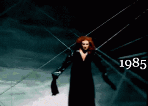a woman in a black dress is standing in a dark room with the year 1985 written on the bottom