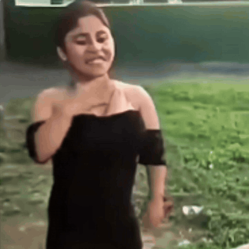A Woman In A Black Dress Is Standing In A Field With Her Hand On Her Chest . GIF