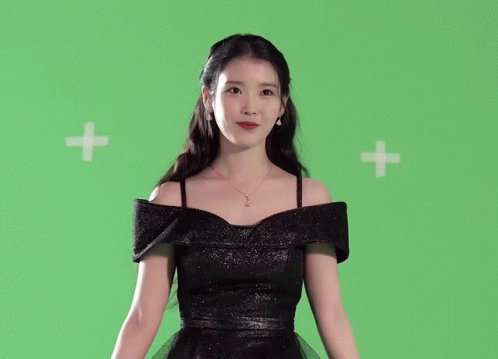a woman in a black dress is standing in front of a green background