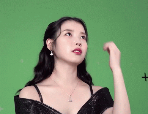 a woman in a black dress is standing in front of a green screen with a plus sign on it