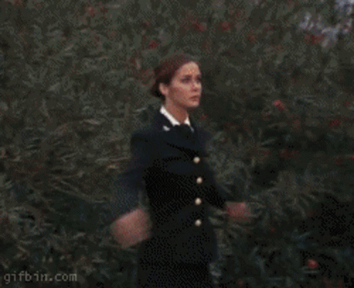 A Woman In A Black Dress Is Standing In Front Of A Red Circle That Says Gifbin.com On It GIF