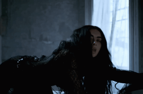 A Woman In A Black Dress Is Standing In Front Of A Window GIF