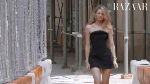 A Woman In A Black Dress Is Walking Down A Street . GIF