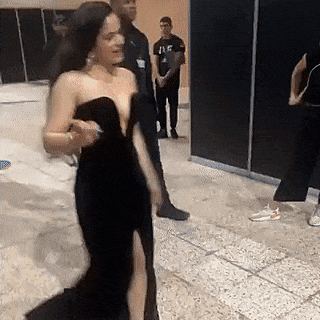 A Woman In A Black Dress Is Walking In A Room . GIF