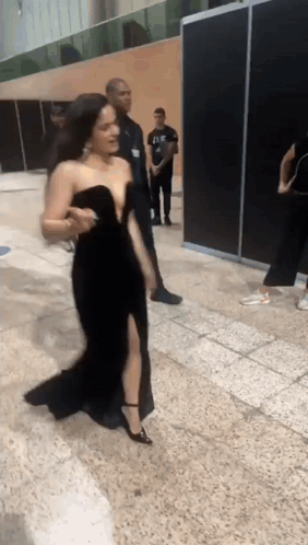 A Woman In A Black Dress Is Walking On A Tiled Floor GIF