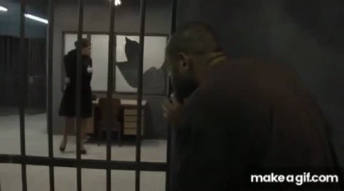 A Woman In A Black Dress Is Walking Through A Jail Cell . GIF