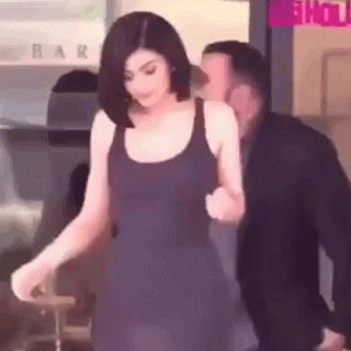 A Woman In A Black Dress Is Walking With A Man In A Suit Behind Her . GIF