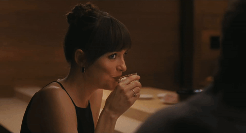 A Woman In A Black Dress Sits At A Table GIF