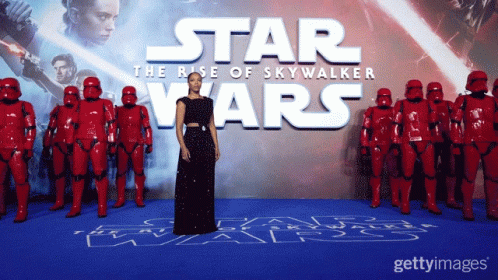 A Woman In A Black Dress Stands In Front Of A Star Wars Poster GIF