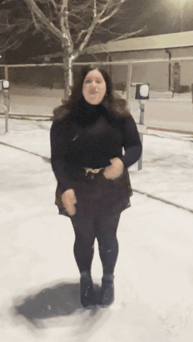 A Woman In A Black Dress Stands In The Snow GIF