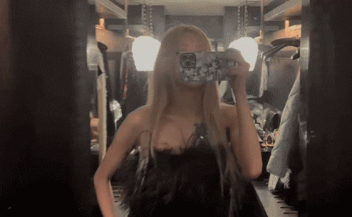 A Woman In A Black Dress Takes A Picture Of Herself In A Mirror GIF