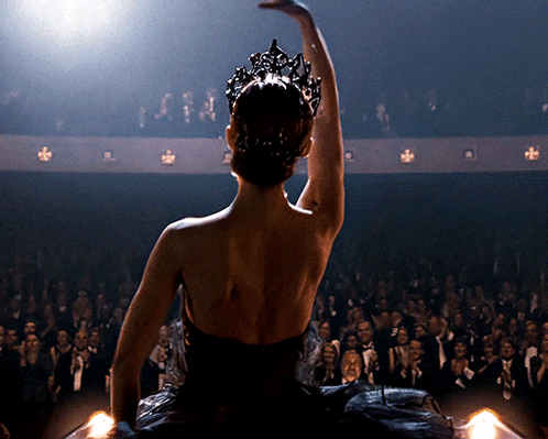 A Woman In A Black Dress With A Crown On Her Head Is Dancing In Front Of A Crowd GIF