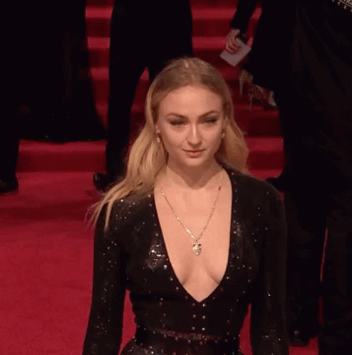 A Woman In A Black Dress With A Plunging Neckline Is Walking Down A Red Carpet . GIF