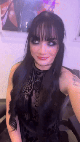 A Woman In A Black Dress With A Tattoo On Her Arm Is Smiling GIF