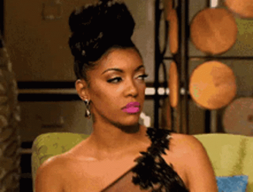 A Woman In A Black Dress With Pink Lipstick Is Sitting On A Chair . GIF