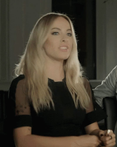 A Woman In A Black Dress With Sheer Sleeves GIF