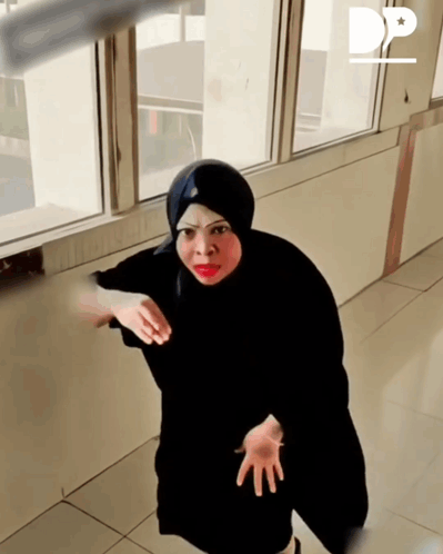 a woman in a black hijab is standing in front of a window with the letter d on the bottom right