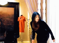 A Woman In A Black Hoodie Stands In Front Of A Picture GIF