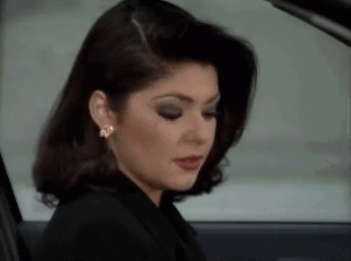 A Woman In A Black Jacket And Earrings Is Sitting In A Car Looking Out The Window . GIF