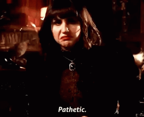 A Woman In A Black Jacket And Necklace Is Standing In A Dark Room And Talking . GIF