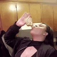A Woman In A Black Jacket Is Drinking From A Bottle Of Beer . GIF
