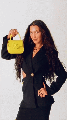 A Woman In A Black Jacket Is Holding A Small Yellow Bag GIF