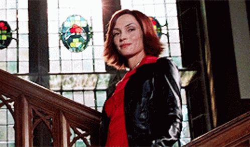A Woman In A Black Jacket Is Standing On A Set Of Wooden Stairs In Front Of A Stained Glass Window GIF