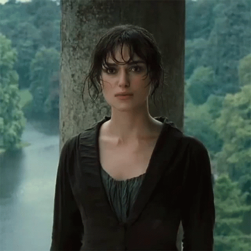 A Woman In A Black Jacket Stands In Front Of A Body Of Water GIF