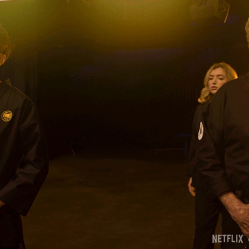 A Woman In A Black Karate Uniform Is Standing In Front Of A Netflix Sign GIF
