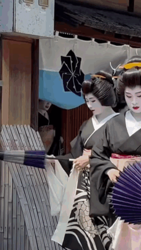 A Woman In A Black Kimono Is Holding A Fan In Front Of A Blue And White Flag With A Cross On It GIF