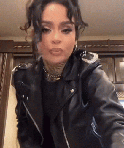 a woman in a black leather jacket is standing in a kitchen .