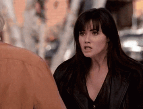 A Woman In A Black Leather Jacket Is Standing Next To A Man In An Orange Shirt . GIF