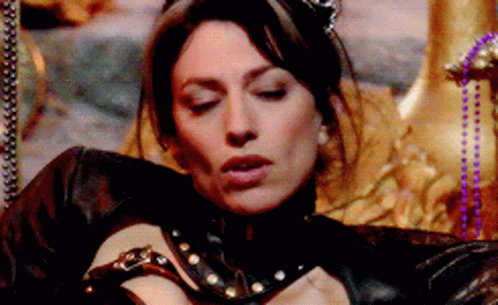A Woman In A Black Leather Outfit Is Laying On A Throne With Her Eyes Closed GIF