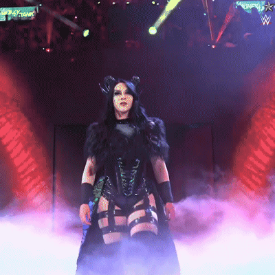 A Woman In A Black Outfit Stands On A Stage With A Sign That Says ' Wwe ' On It GIF