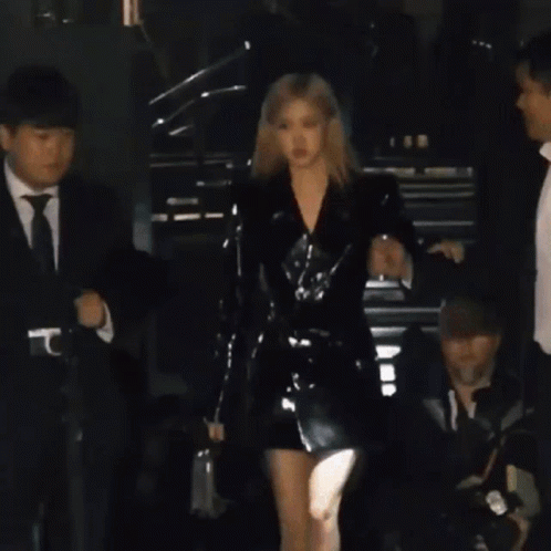 A Woman In A Black Sequined Dress Is Standing In Front Of A Wall With The Word Saint Laurent Written On It . GIF
