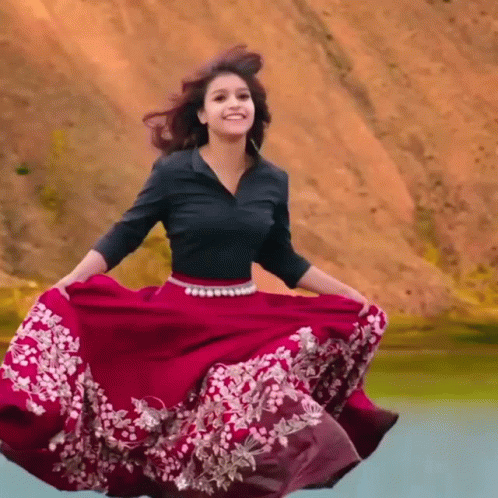 A Woman In A Black Shirt And A Red Skirt Is Smiling GIF