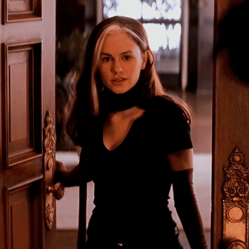 A Woman In A Black Shirt And Black Gloves Stands In A Doorway GIF