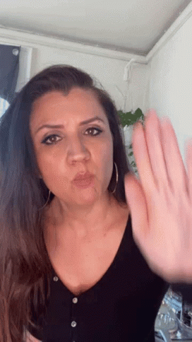A Woman In A Black Shirt Is Blowing A Kiss And Making A Stop Sign With Her Hand GIF