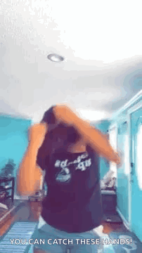 A Woman In A Black Shirt Is Dancing In A Living Room With Her Hands In Her Hair . GIF