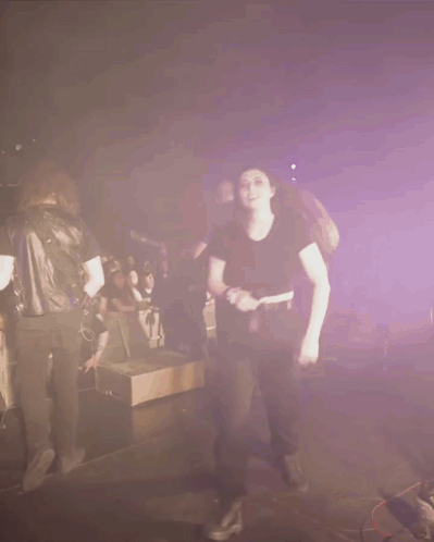 A Woman In A Black Shirt Is Dancing In Front Of A Crowd Of People GIF