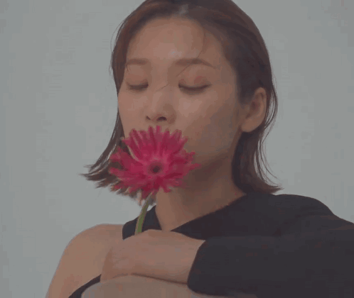 A Woman In A Black Shirt Is Holding A Red Flower In Her Hand GIF