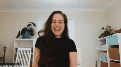 A Woman In A Black Shirt Is Laughing In A Room With The Name Elaniezanetti On The Bottom GIF