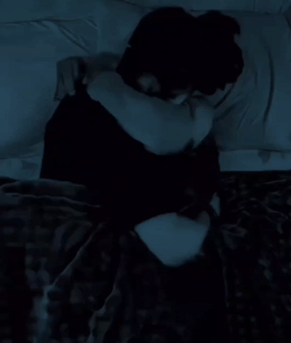 A Woman In A Black Shirt Is Laying On A Bed With A White Pillow GIF
